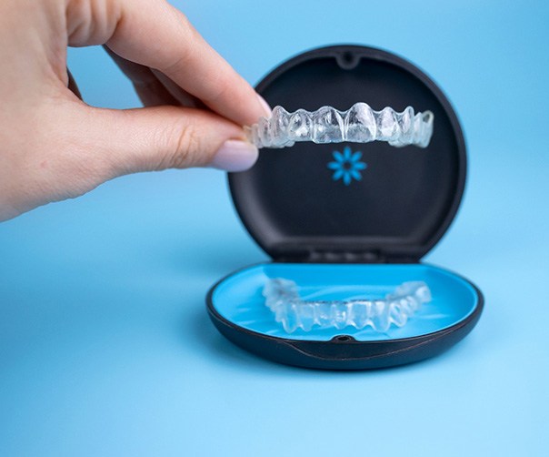 Hand plucking Invisalign tray from carrier case with light blue background