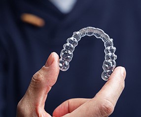 Dentist in navy scrubs holding Invisalign tray between two fingers
