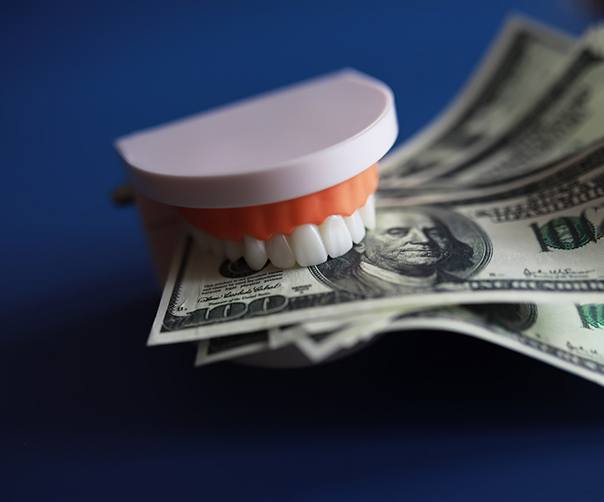 Model dentures biting down on hundred dollar bills