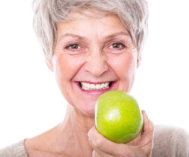 Older woman with dentures holding an apple. 