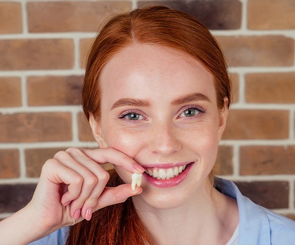 Smiling woman holding up extracted tooth