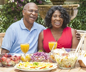 couple sitting outside at a table with various foods and drinks 