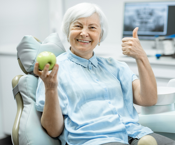 Woman with dentures giving thumbs up and smiling