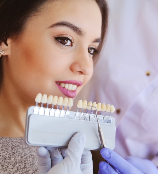 Woman's smile compared with tooth color chart during cosmetic dentistry visit