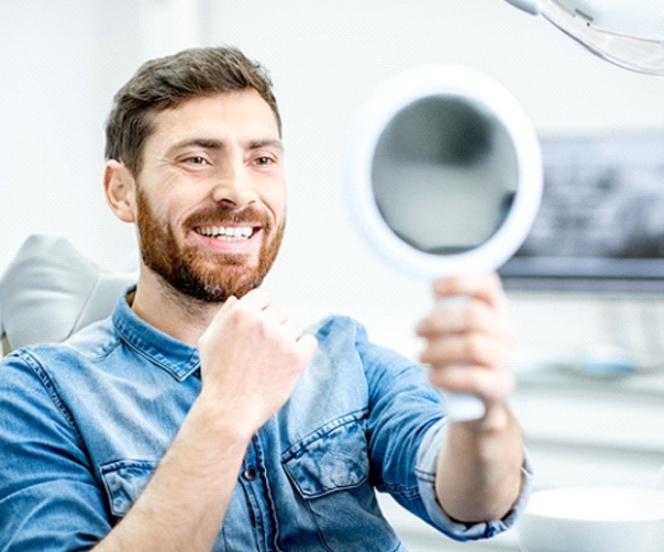 Man smiling while looking in mirror at cosmetic dentist's office