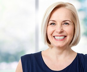 Woman smiling with veneers in blue shirt with window in background